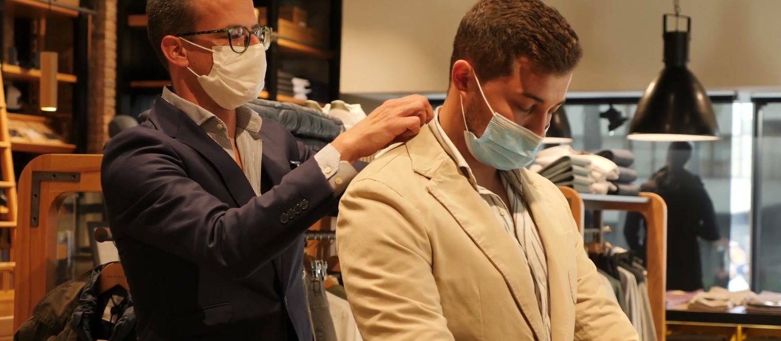 A sales associate helping a shopper into a jacket on a store floor.